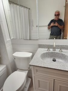 Finished bathroom remodeling view with a worker reflected in the mirror