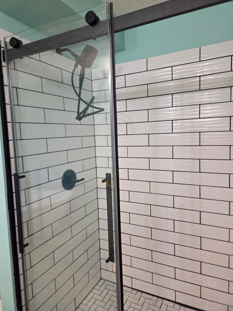 Walk-in tile shower with a black-framed glass enclosure, recessed niche, and built-in seat