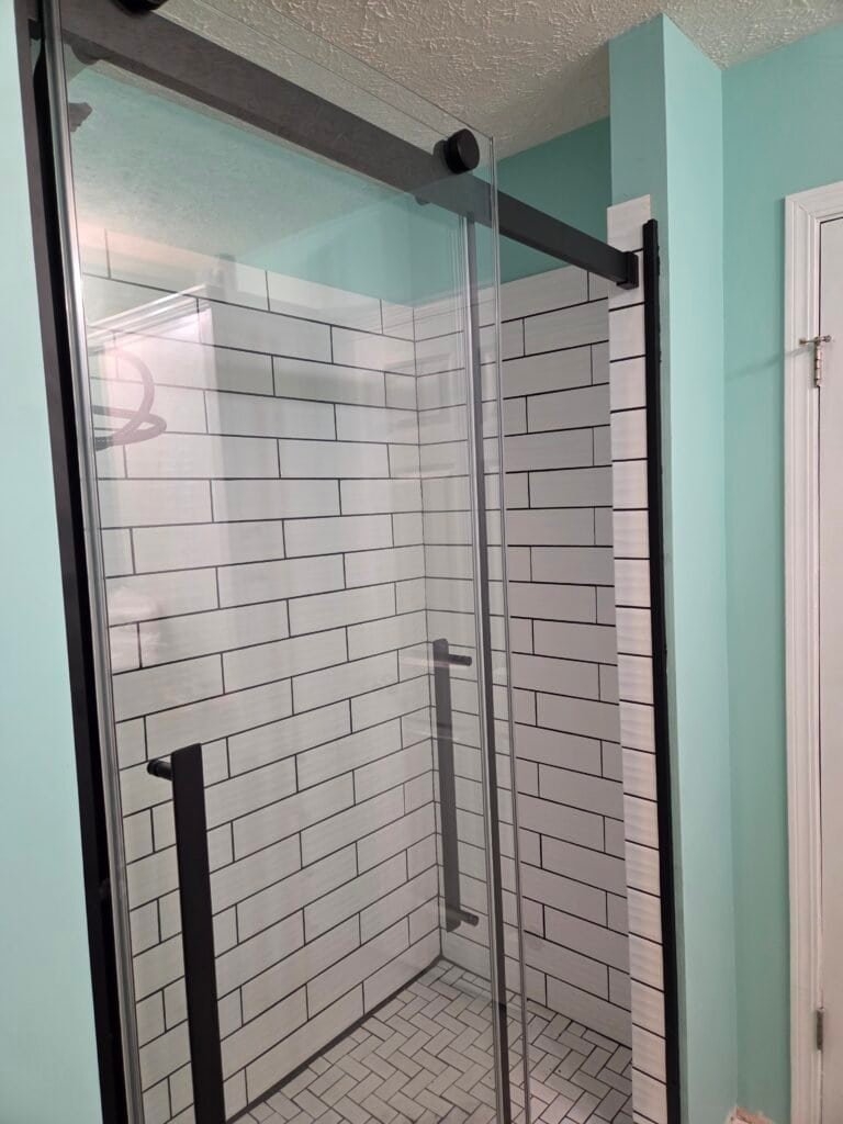 Walk-in tile shower with a black-framed glass enclosure, recessed niche, corner shelves, and built-in seat